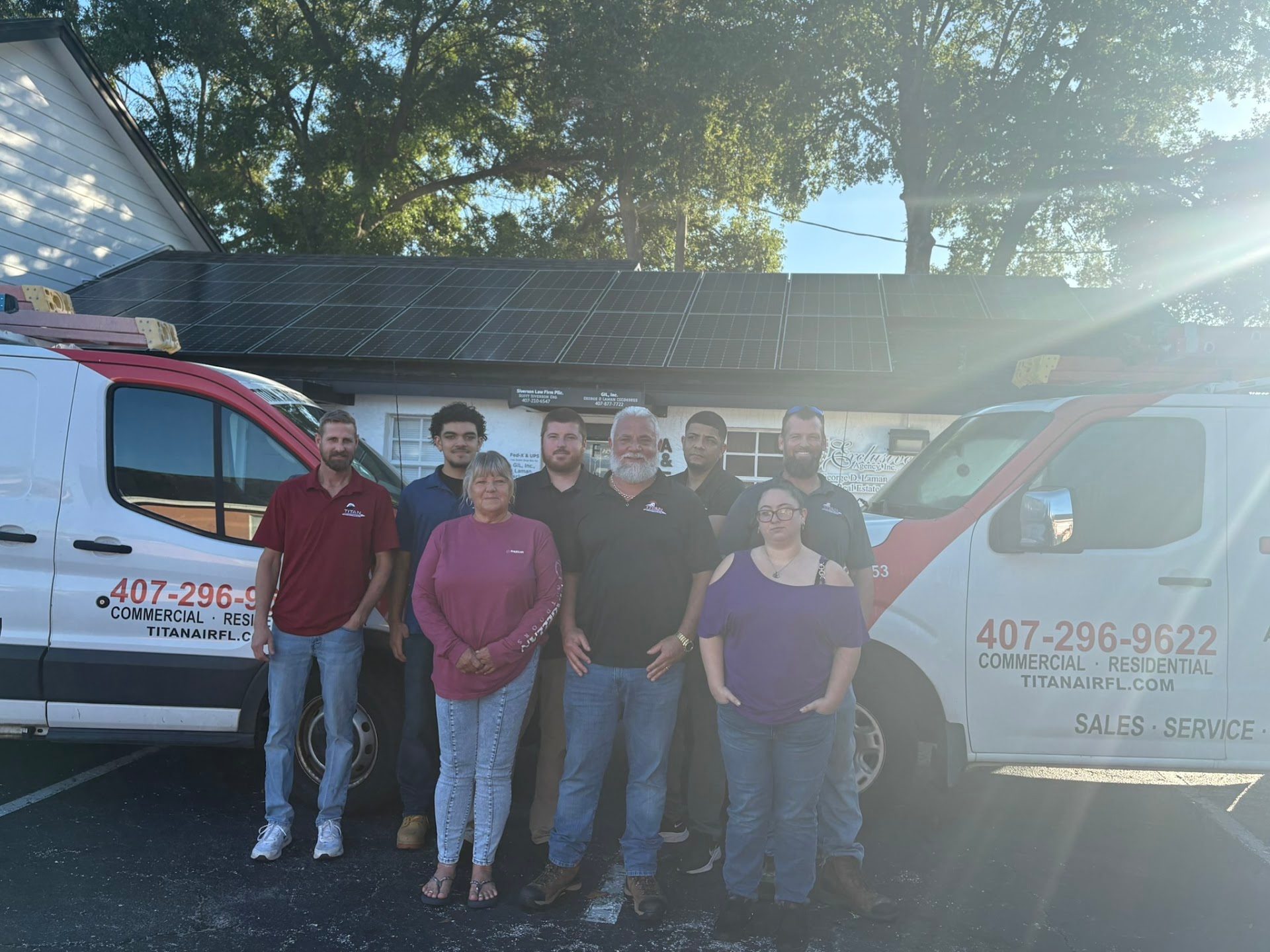 Eight members of the Titan Air Conditioning and Heating team in front of two branded service vans